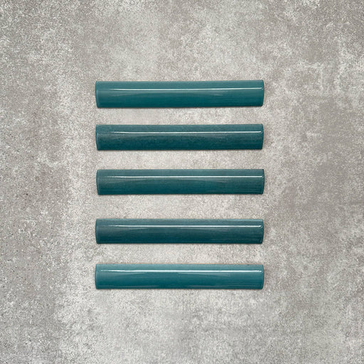 Flatlay von Zellige Pfauengrün Bullnose-Keramikfliesen im marokkanischen Stil im Format 3 × 20 cm, mit abgerundetem Kantenprofil, tief blau-grüner Glasur und feiner tonaler Variation auf neutralem Hintergrund.