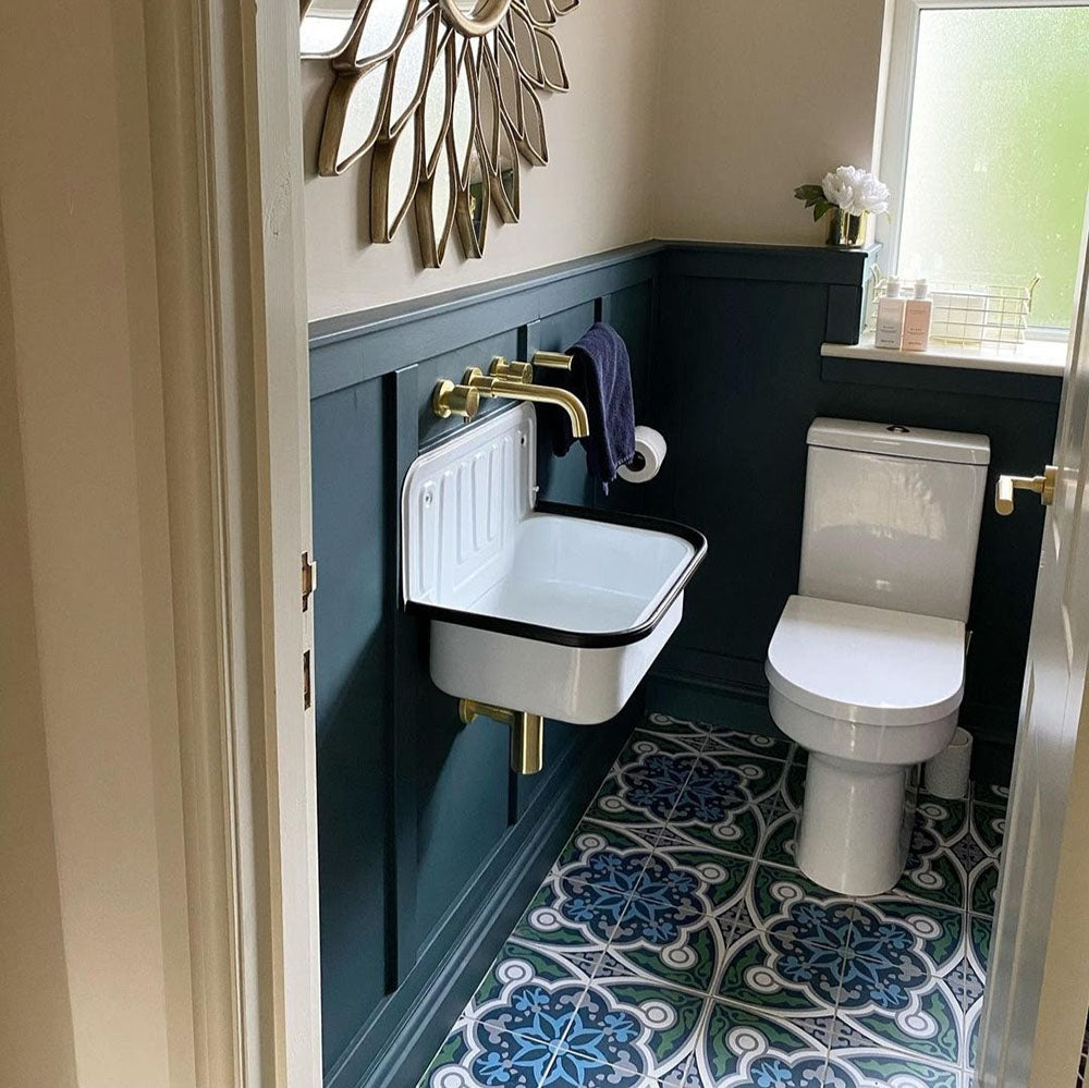 Badezimmer mit Berlin Stadt Bodenfliesen im Format 20 × 20 cm im viktorianisch-marokkanisch inspirierten Stil. Kombiniert mit dunkelblauer Wandverkleidung, Messingarmaturen und einem kompakten Wandwaschbecken entsteht ein markanter, gemusterter Badezimmerboden.