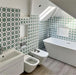 Badezimmerinterieur mit Agadir Grün Fliesen im marokkanischen Stil im Format 20 × 20 cm aus Feinsteinzeug, eingesetzt als Wandfliesen mit sich wiederholendem geometrischem Sternmuster in Grün und Weiß. Kombiniert mit freistehender Badewanne, moderner Sanitärausstattung und einer hellen, luftigen Raumgestaltung.