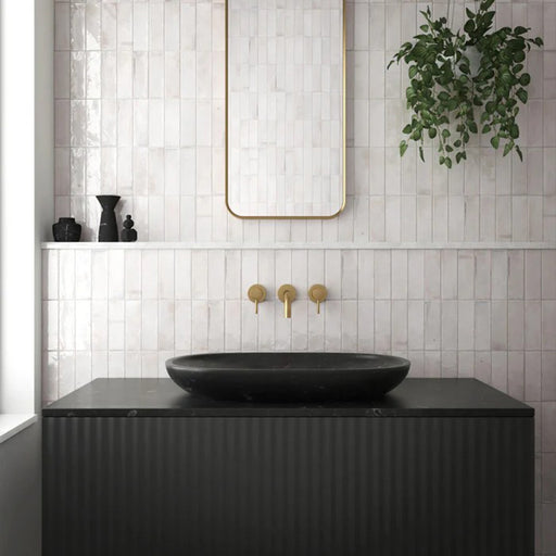 Badezimmerwand mit Saigon Weiß Brick Wandfliesen im marokkanisch inspirierten Stil. Glänzende Keramikfliesen im Format 5,1 × 16,1 cm in sanften Weißtönen, kombiniert mit einem schwarzen Waschtisch, Messingarmaturen und einem minimalistischen Spiegel.