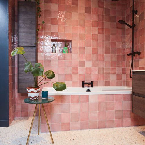 Badezimmer mit Zellige Rosa Quadrat Keramik-Wandfliesen im marokkanischen Stil im Format 13,2 × 13,2 cm, in sanften Blush- und Pudertönen verlegt. Die klassische Rasterverlegung rund um Badewanne und Duschbereich, kombiniert mit einer Nische, schwarzen Armaturen und einem Boden in Terrazzo-Optik, bringt die feine Farbvariation und die handgefertigte Zellige-Optik besonders schön zur Geltung.