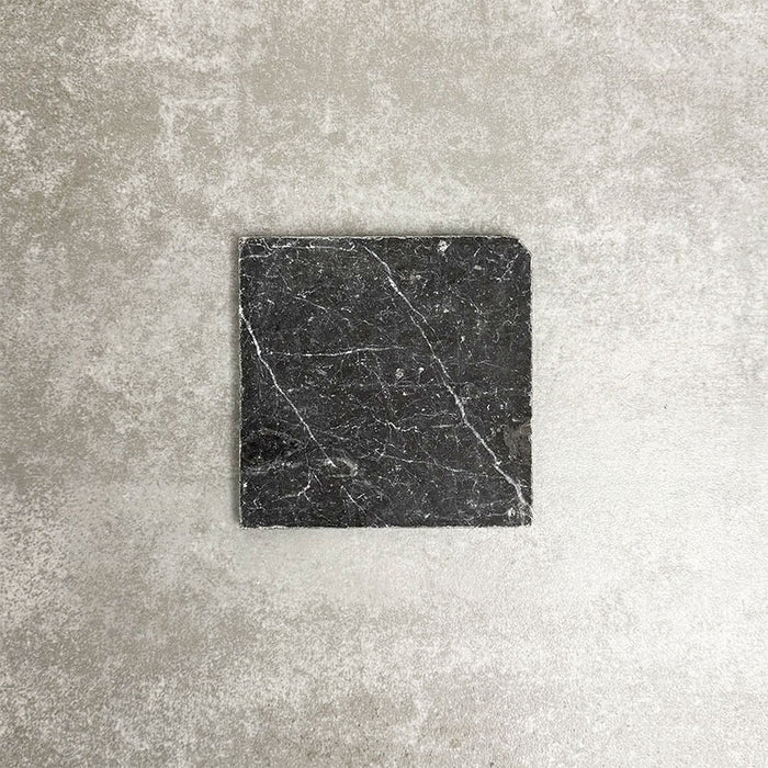 Single Fayrouz Black 15.2x15.2cm natural marble tile with a tumbled finish, featuring deep charcoal tones and striking natural veining, displayed against a neutral textured background in a clean product setting.