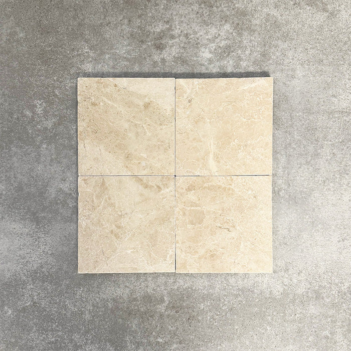 Vier Fayrouz Cappuccino 15,2 × 15,2 cm Naturmarmorfliesen mit getrommelter Oberfläche nebeneinander angeordnet, die sanften Cremetöne, feine Maserung und natürliche Variation vor einem neutralen, strukturierten Hintergrund zeigen.