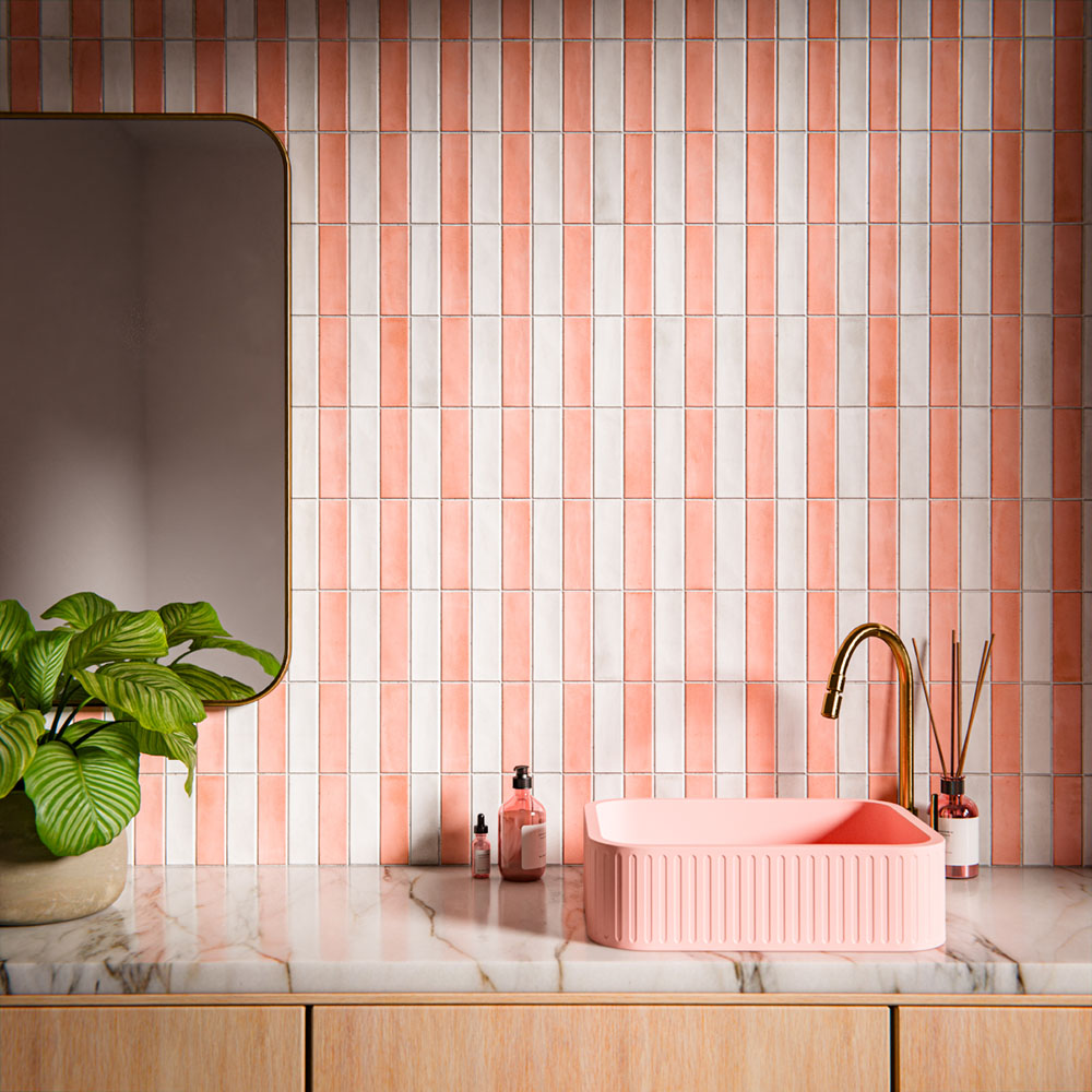 Waschtischbereich im Badezimmer mit Benomar Ziegelfliesen im marokkanischen Stil in sanften Rosé- und Elfenbeintönen, vertikal als Statement-Wand verlegt und kombiniert mit einem geriffelten rosafarbenen Waschbecken, einer Armatur in gebürstetem Messing, einer Marmoroberfläche und Pflanzen.