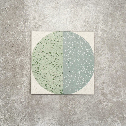 Produktpräsentation der Eclipse Salvia Dekorfliesen im Terrazzo-Look im Format 20 × 20 cm in sanften Salbei- und Grautönen, mit geometrischen Kreisdesigns und gesprenkelten Details vor einem Hintergrund in strukturierter Betonoptik.
