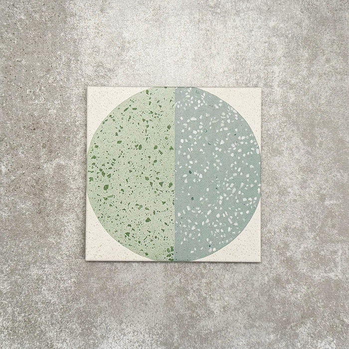 Produktpräsentation der Eclipse Salvia Dekorfliesen im Terrazzo-Look im Format 20 × 20 cm in sanften Salbei- und Grautönen, mit geometrischen Kreisdesigns und gesprenkelten Details vor einem Hintergrund in strukturierter Betonoptik.
