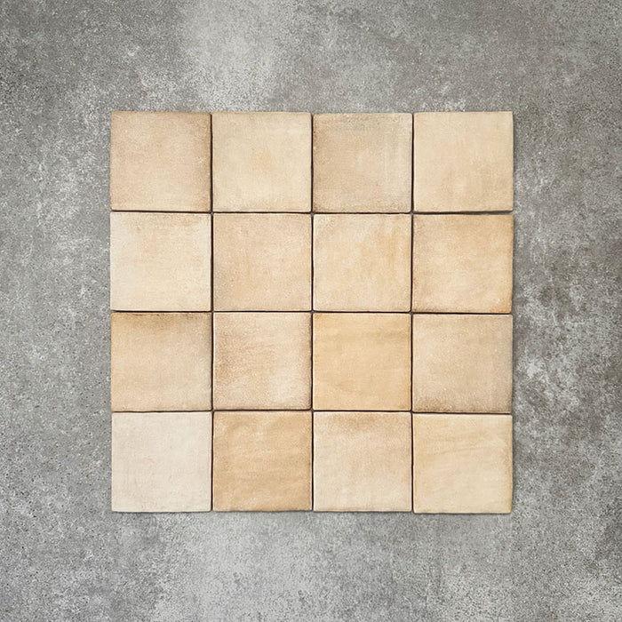 Flatlay von Zellige Sandbeige Matt Quadrat Keramikfliesen im marokkanischen Stil im Format 10 × 10 cm, in warmen Beige- und Sandtönen. Die Fliesen sind in einem schlichten Raster auf strukturiertem grauem Hintergrund angeordnet, um die feine Farbvariation und die handgefertigte Zellige-Oberfläche zu zeigen.