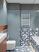 Badezimmer mit Melodie Rock Terrazzo Blau 60 × 60 cm Feinsteinzeug-Wand- und Bodenfliesen mit sanft blauer Basis und großen weißen Zuschlägen, kombiniert mit strukturierten blauen Wandfliesen, weißen Armaturen und einem modernen Gesamtbild.