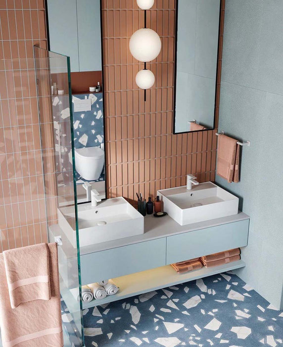 Badezimmer mit Melodie Rock Terrazzo Blau 60 × 60 cm Feinsteinzeug-Bodenfliesen mit sanft blauer Basis und großen weißen Zuschlägen, kombiniert mit vertikal verlegten Terrakotta-Wandfliesen, schwebendem Waschtisch und einem klaren, designorientierten Look.