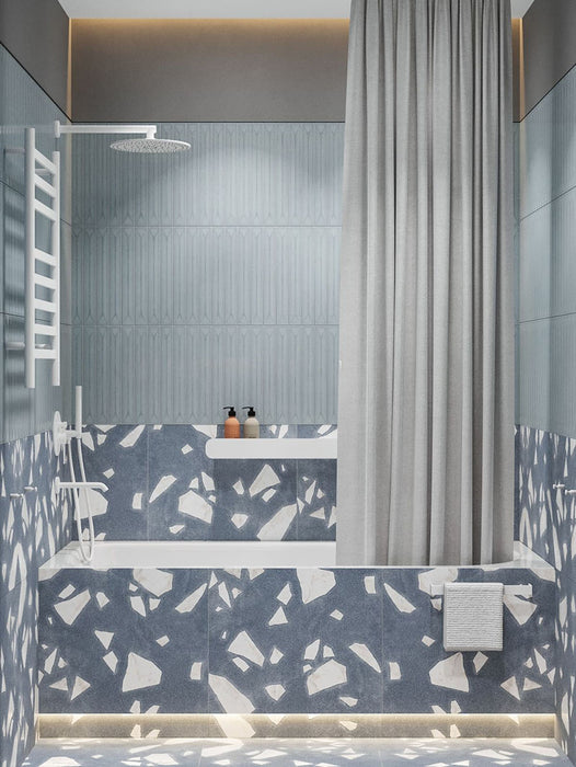 Badezimmer mit Melodie Rock Terrazzo Blau 60 × 60 cm Feinsteinzeug-Wand- und Bodenfliesen mit sanft blauer Basis und großen weißen Zuschlägen, kombiniert mit strukturierten blauen Wandfliesen, weißen Armaturen und weicher, indirekter Beleuchtung.