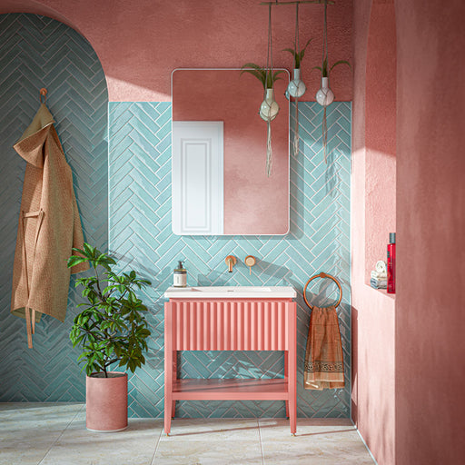 Modernes Badezimmer mit Nomad Aqua glänzenden Brick-Wandfliesen, im Fischgrätmuster verlegt, kombiniert mit rosafarbenen, gekalkten Wänden, einem geriffelten Waschtischunterschrank in Koralle, Armaturen in gebürsteter Messingoptik, hängenden Pflanzgefäßen und Bodenfliesen in heller Steinoptik für ein verspieltes, modernes Interior.