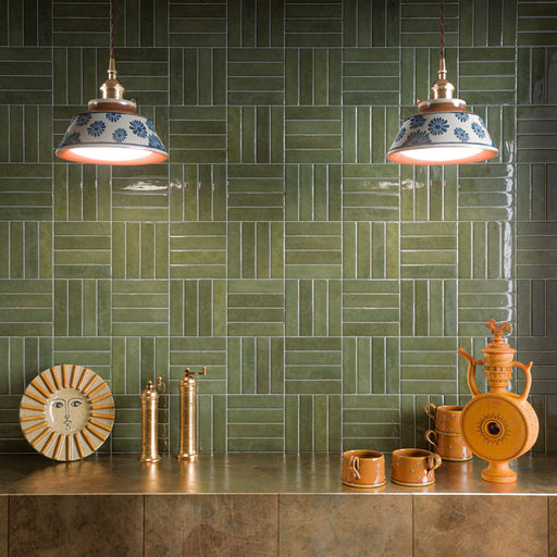 Moderne Küchenrückwand mit Nomadin Salbeigrün glänzenden Brick-Wandfliesen, im Korbflechtmuster verlegt, kombiniert mit bronzefarbenen Arbeitsplatten, Armaturen in Messingoptik, keramischen Pendelleuchten und warmen Terrakotta-Accessoires für ein ausdrucksstarkes Interior voller Charakter.
