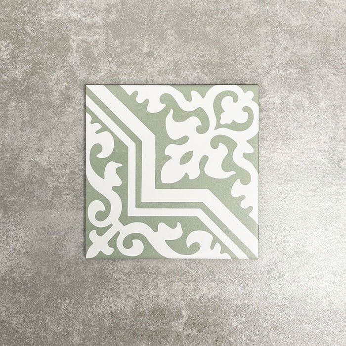 Einzelne Berlin Trondite Grün Keramikfliese im Format 20 × 20 cm im viktorianisch-marokkanisch inspirierten Stil mit filigranem weißem Ornamentmuster auf einem sanften salbeigrünen Hintergrund, dargestellt vor einem neutralen, strukturierten Hintergrund.
