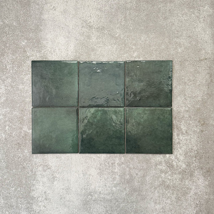 Flatlay von Zellige Königliches Grün Quadrat Keramikfliesen im marokkanischen Stil im Format 13,2 × 13,2 cm, in kräftigen, tiefen Grüntönen. Im schlichten Raster auf strukturiertem grauem Hintergrund arrangiert, um die glänzende Glasur, natürliche Farbvariation und die handgefertigte Zellige-Optik hervorzuheben.