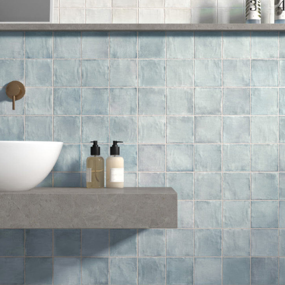 Badezimmerwand mit Zellige Sky Blue Matt Wandfliesen im Format 10 × 10 cm im Moroccan Style, in sanften Blautönen mit dezenten Farbvariationen und matter Oberfläche, kombiniert mit einem schwebenden Waschtisch und modernen Armaturen in Messingoptik für eine ruhige, spa-inspirierte Atmosphäre.